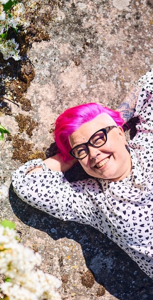 Nainen loikoilee kalliolla hymyillen