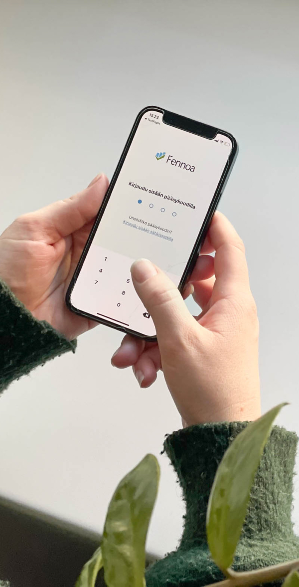 Kädet pitävät puhelinta, jossa Fennoa mobiilisovelluksen kirjautumissivu.